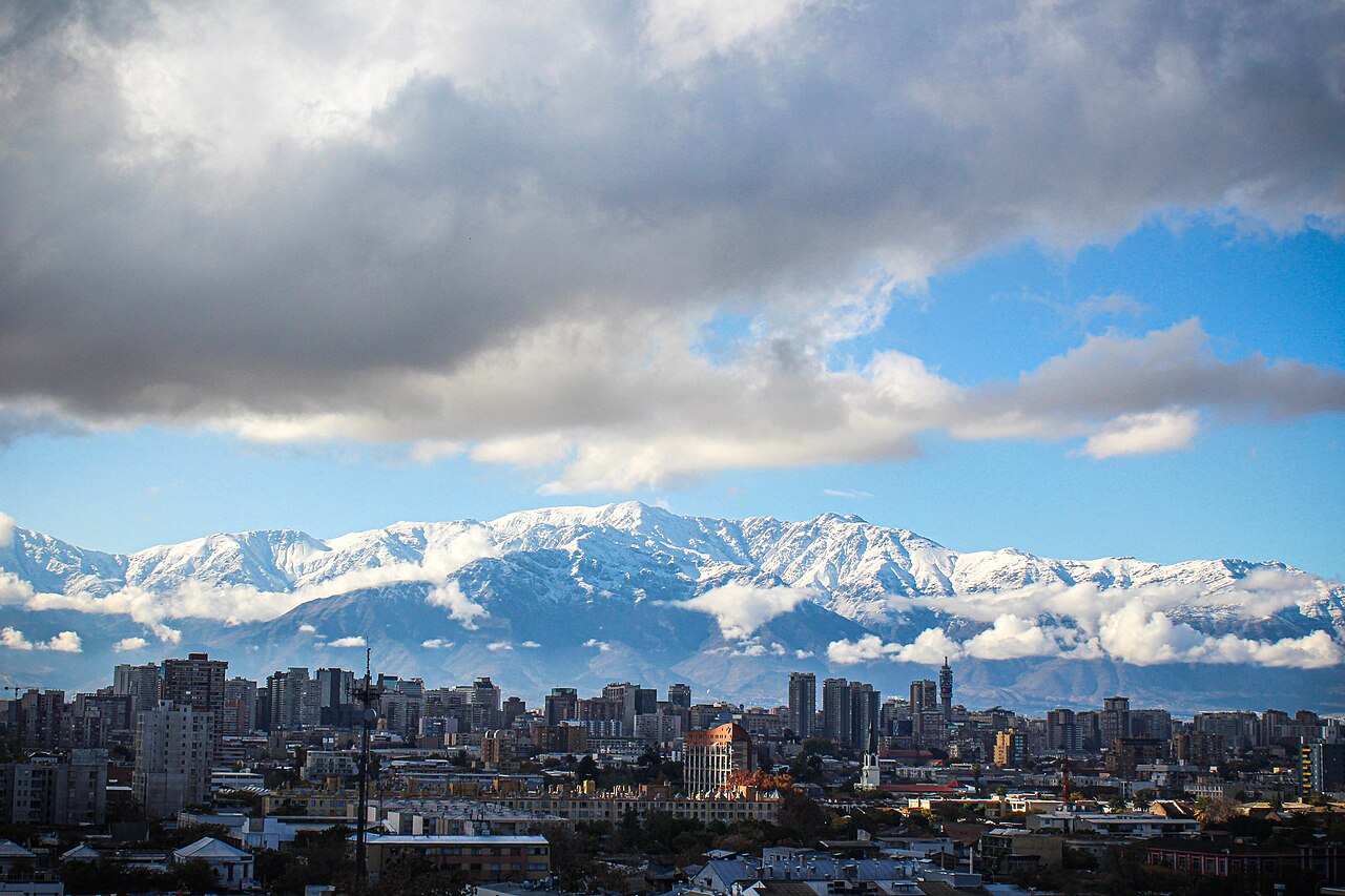 Edificios de Santiago de Chile bajo nubes densas, con la cordillera de los Andes cubierta de nieve al fondo