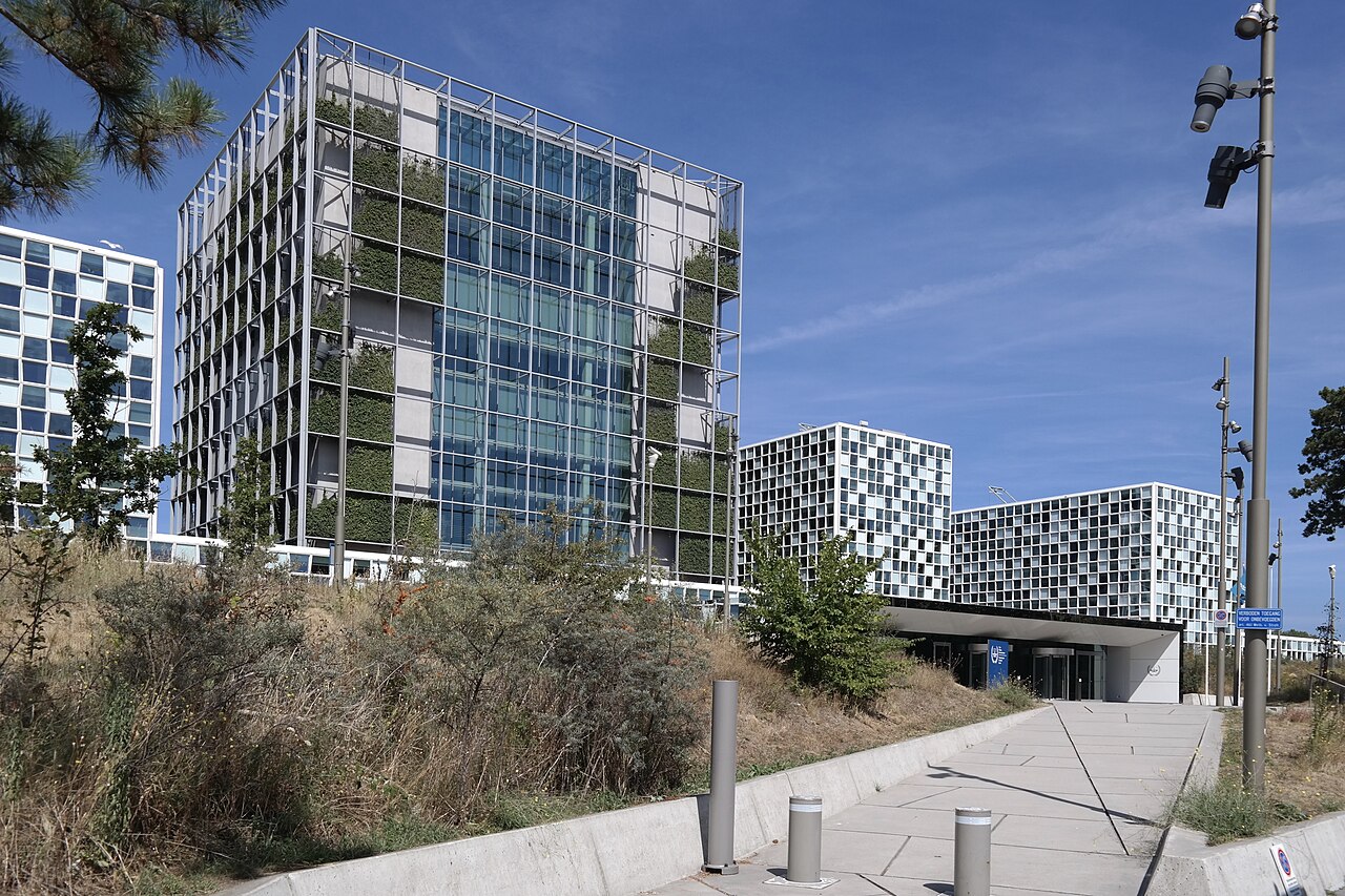 Edificios de la sede de la Corte Penal Internacional en La Haya vistos desde un camino, con la fachada de cristal y vegetación en primer plano
