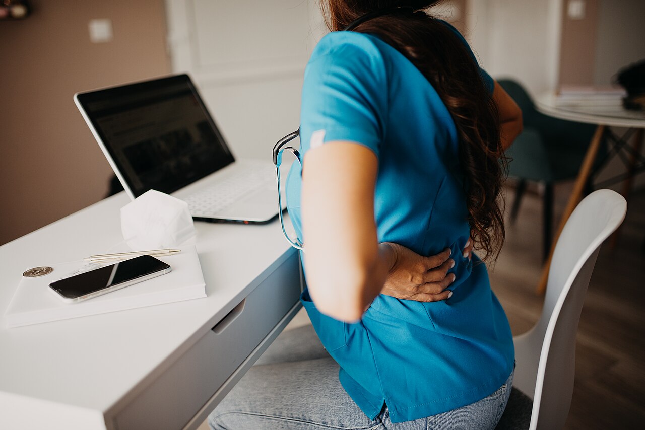 Una persona sentada frente a un escritorio, con dolor de espalda tras pasar mucho tiempo sentada frente al ordenador