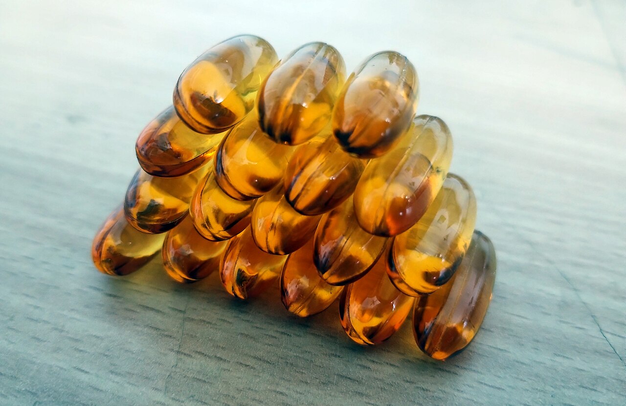 Varias cápsulas de aceite de pescado con omega-3 apiladas sobre una superficie de madera clara