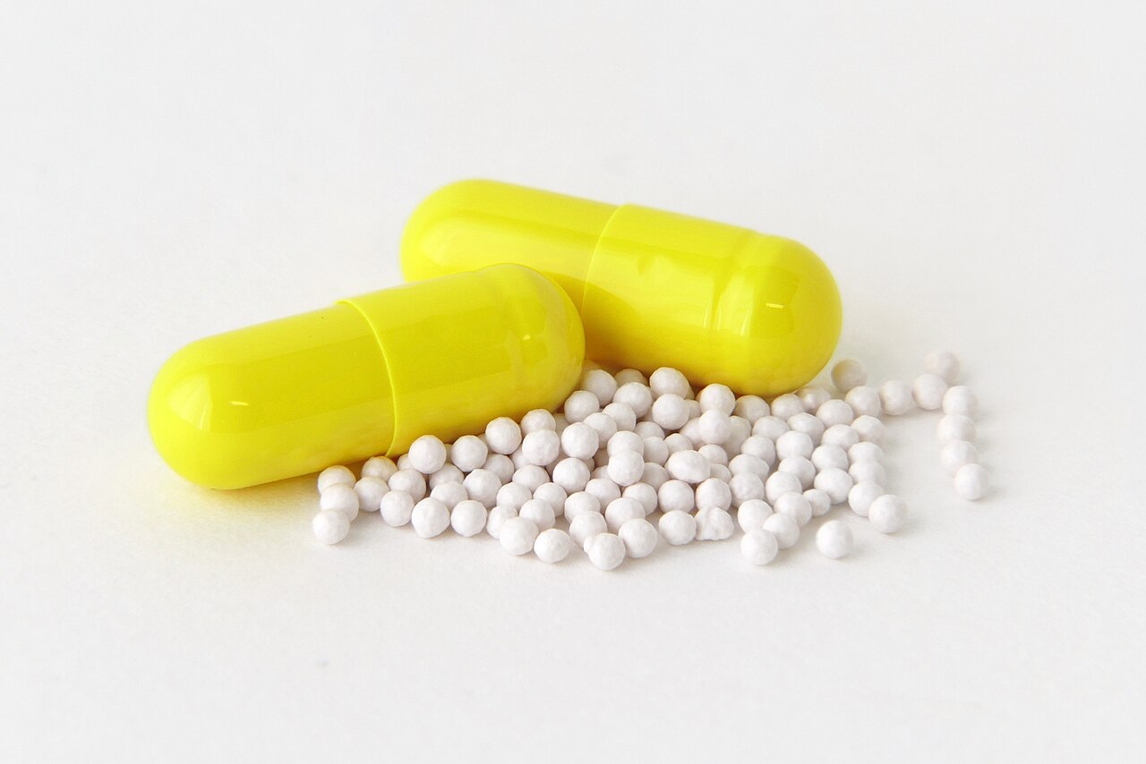 Dos cápsulas amarillas y gránulos blancos de omeprazol sobre un fondo blanco (imagen ilustrativa)