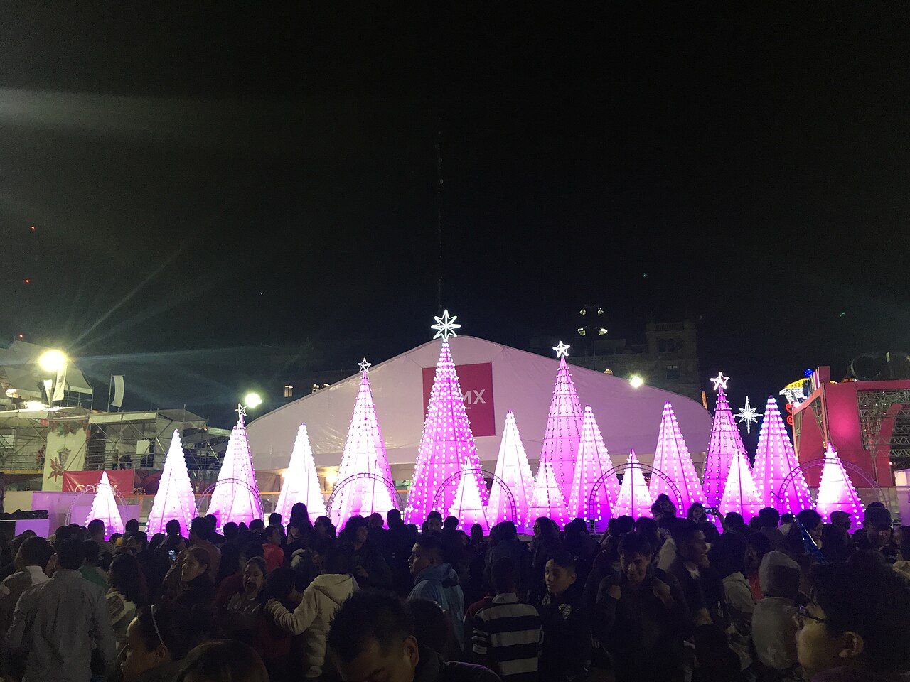 Árboles de luces de Navidad iluminados en la Ciudad de México, con una multitud en primer plano