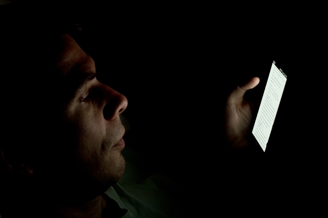 Un hombre mira la pantalla encendida de un teléfono móvil en una habitación completamente a oscuras