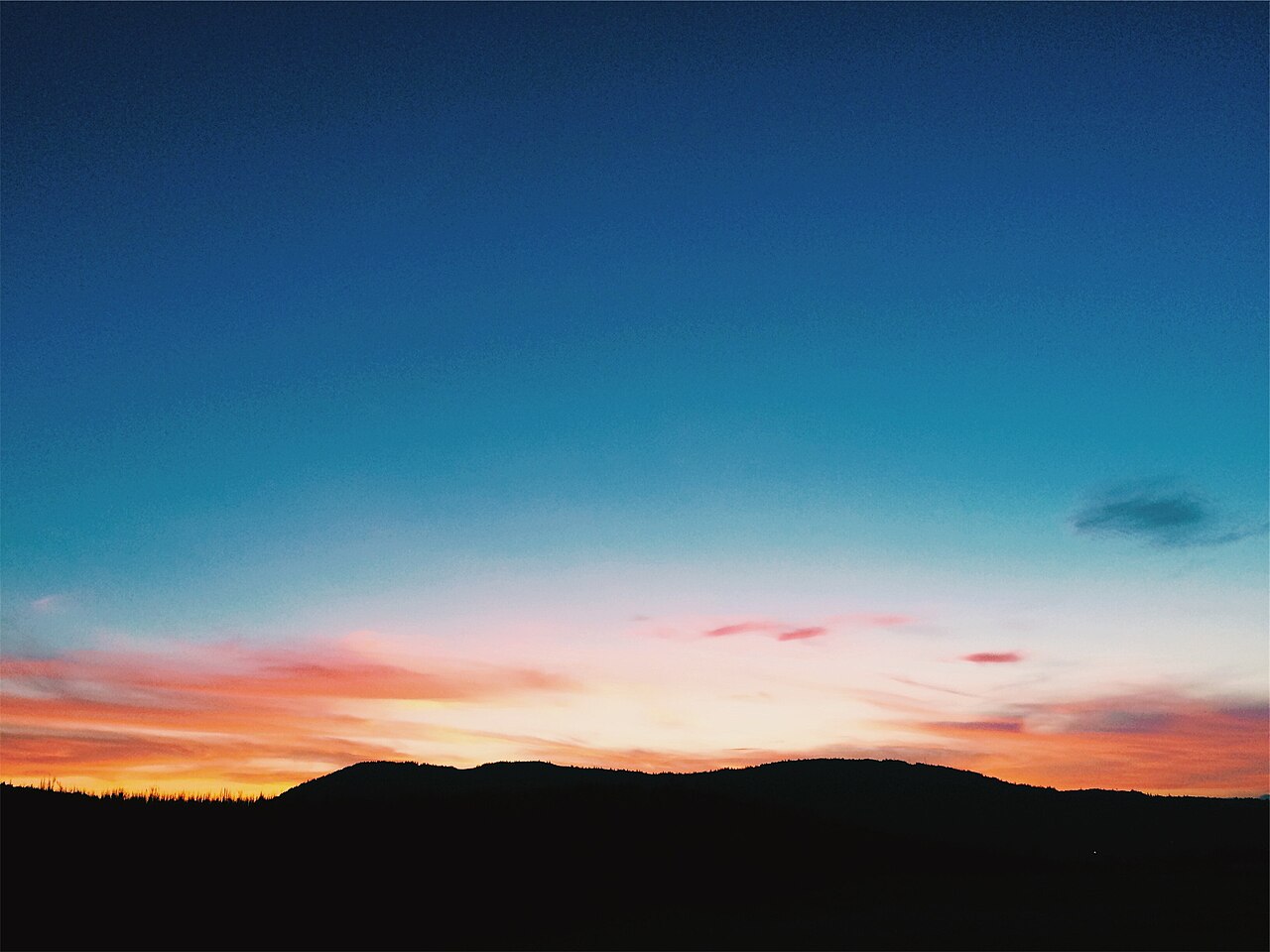 Cielo que pasa del azul intenso arriba al naranja y rosa sobre la silueta oscura de un cerro al atardecer