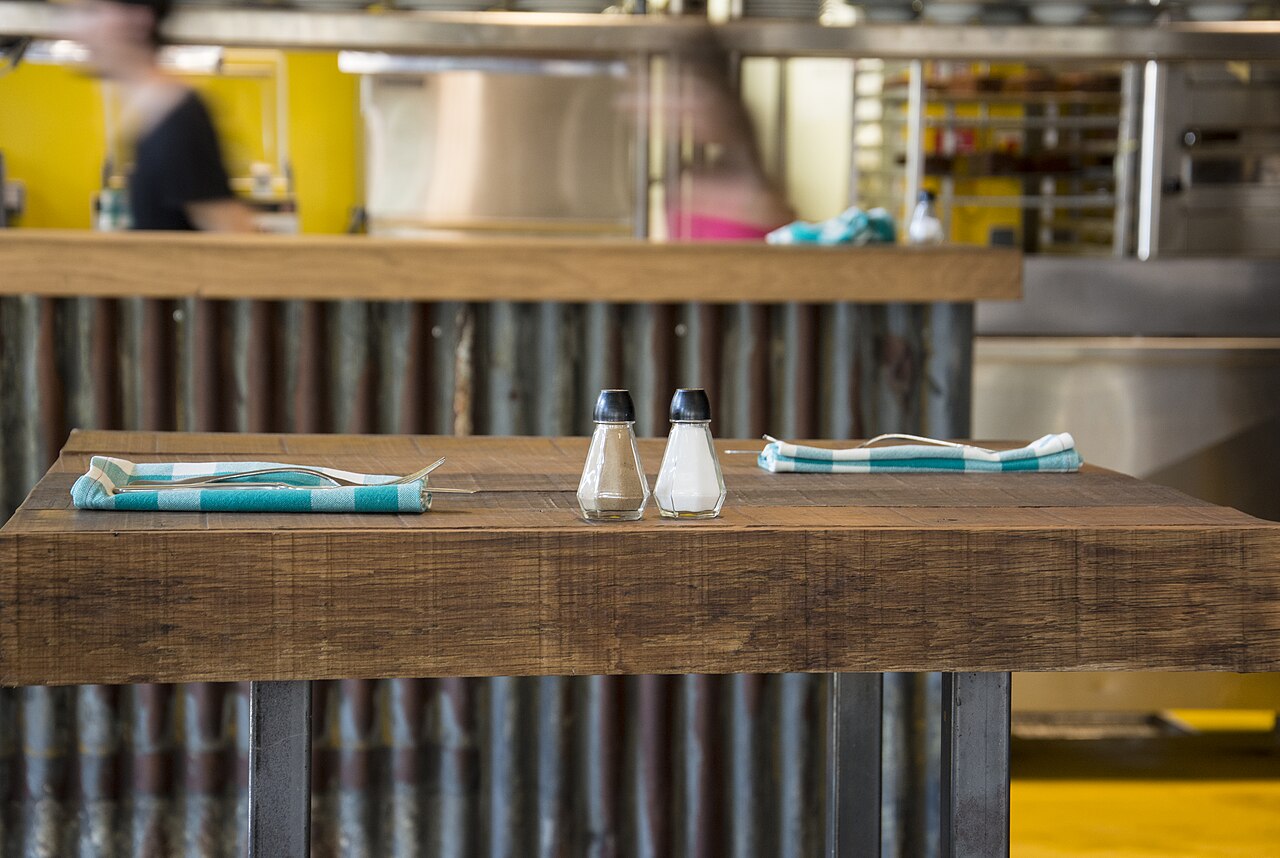 Dos saleros de cristal con tapa negra sobre una mesa de madera de un restaurante