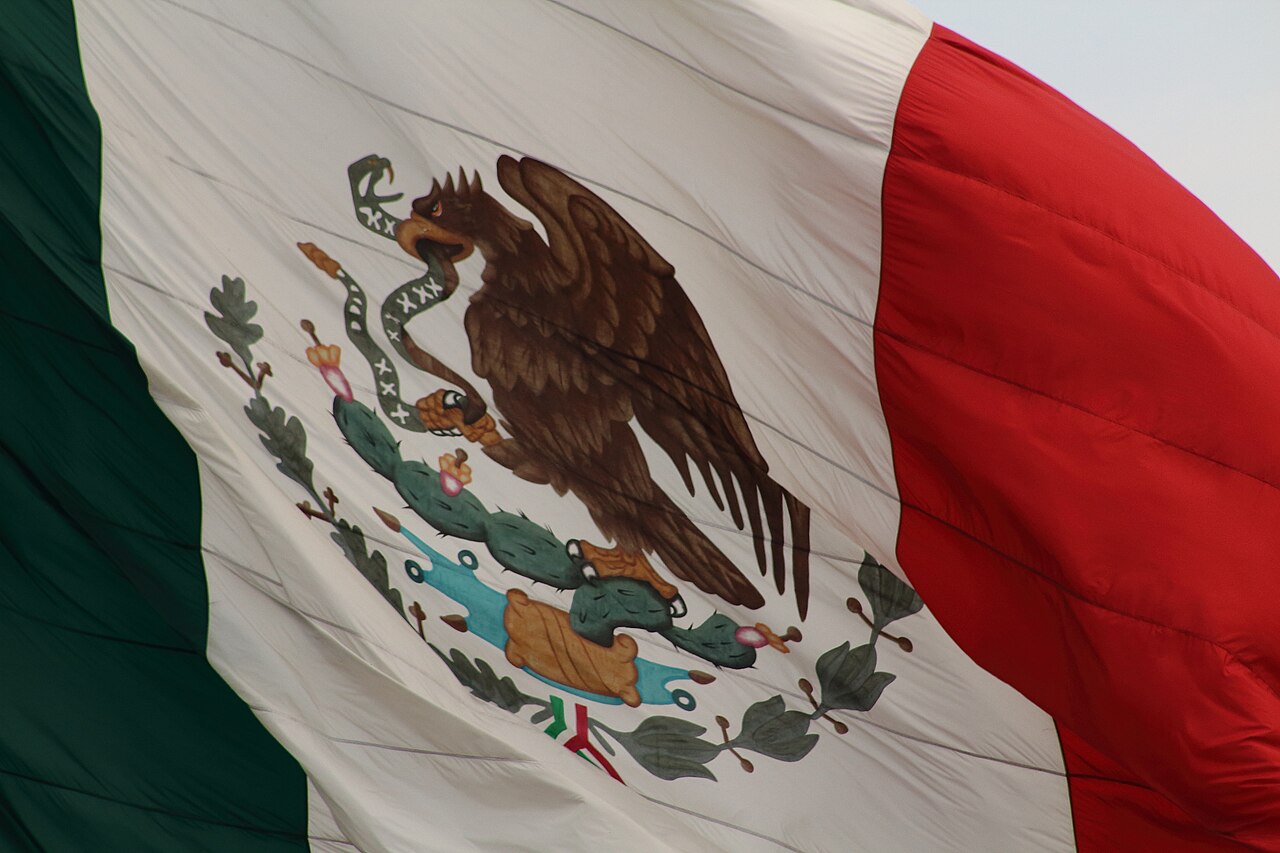 Primer plano de la bandera de México ondeando, con el escudo nacional de un águila sobre un nopal