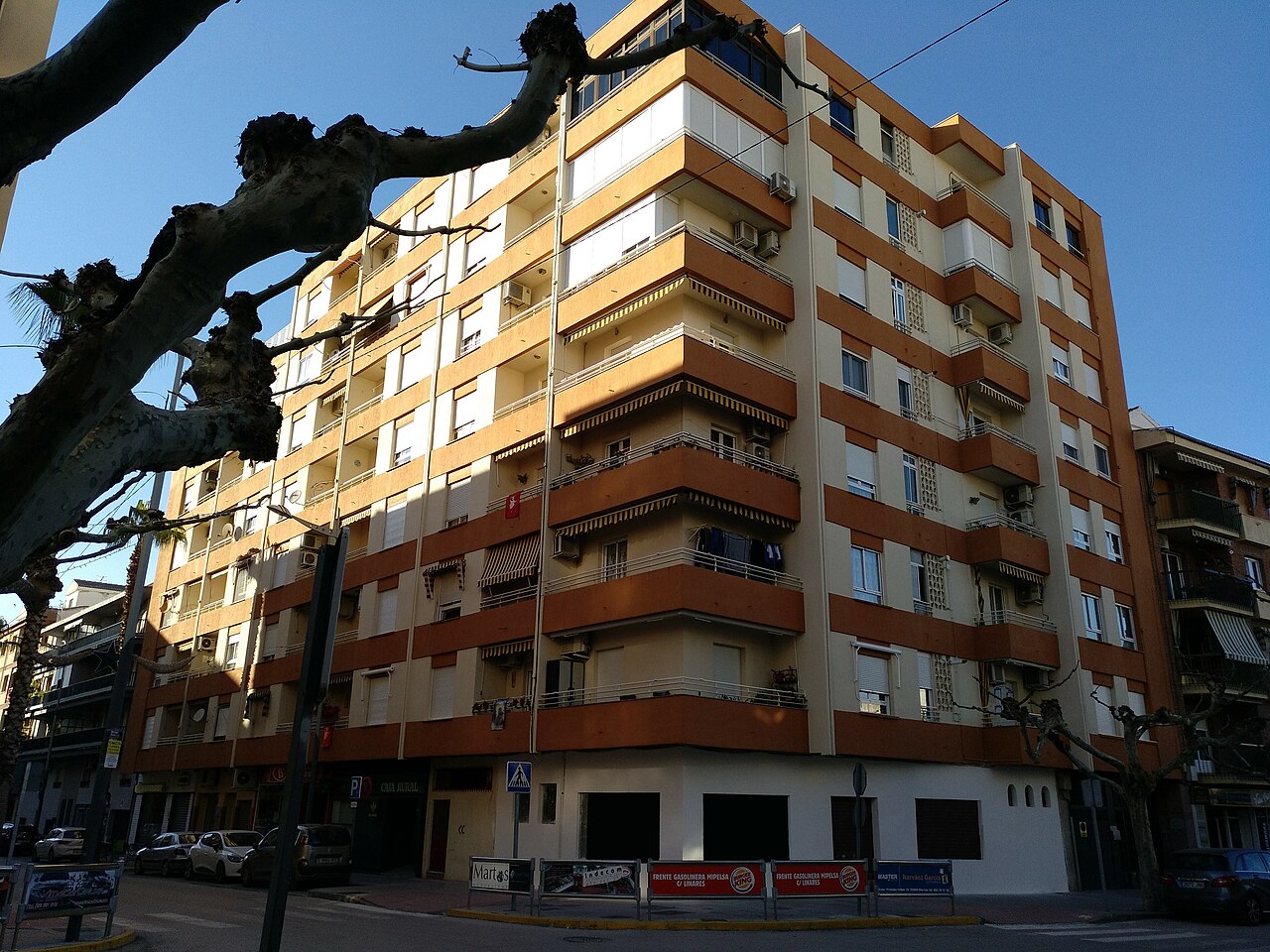 Un bloque de viviendas de varias plantas con balcones, fachada de color amarillo y naranja, en una calle residencial española