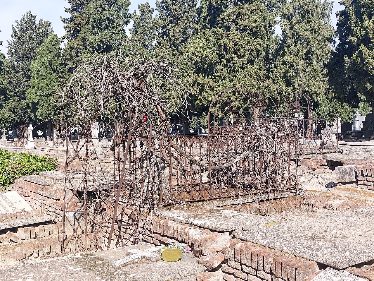Tumba con verja de hierro y arcos entre cipreses en el Cementerio de la Almudena, en Madrid