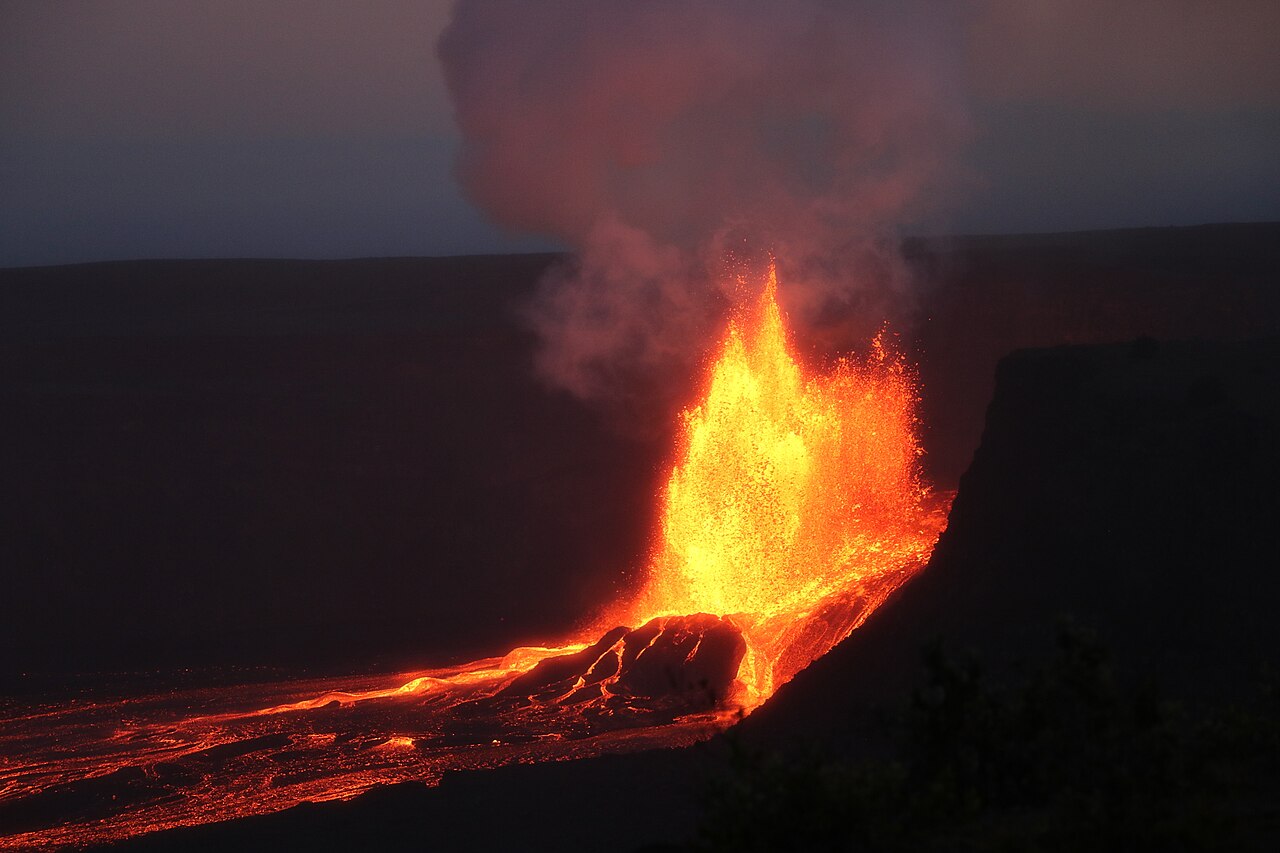 Fuente de lava del volcán Kīlauea al anochecer en el cráter Halemaʻumaʻu, con humo y flujos de lava sobre el suelo del cráter