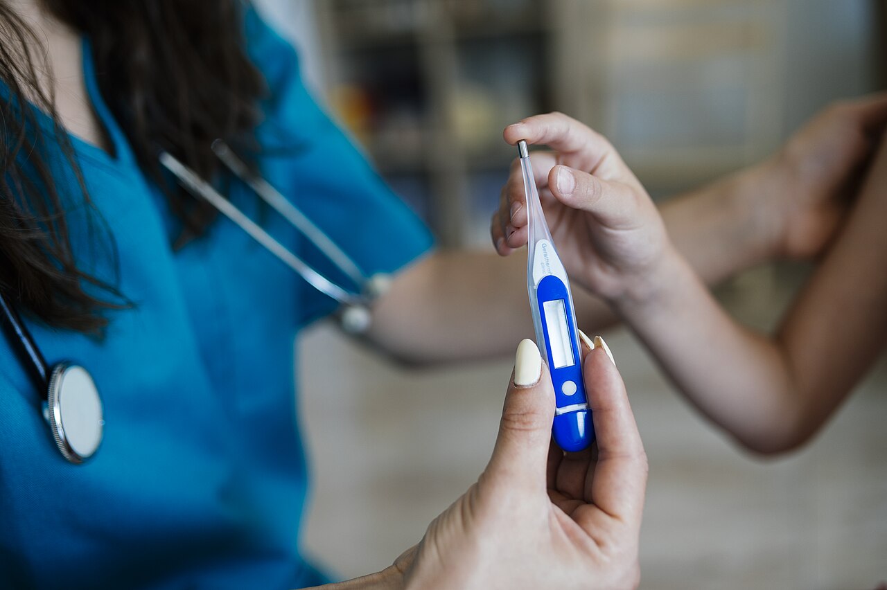 Una profesional sanitaria con estetoscopio sostiene un termómetro digital junto al brazo de un niño