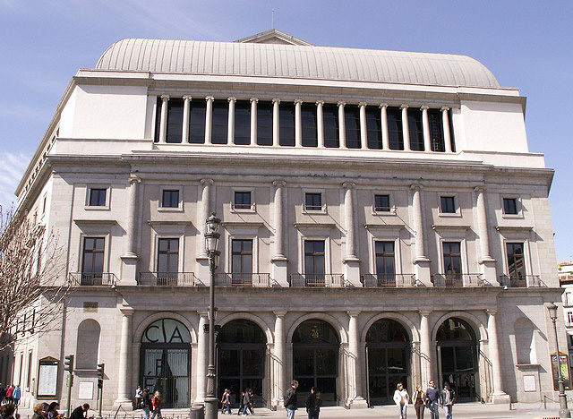 Fachada del Teatro Real de Madrid con su cubierta de cúpula baja y transeúntes ante las puertas de arco en la planta baja