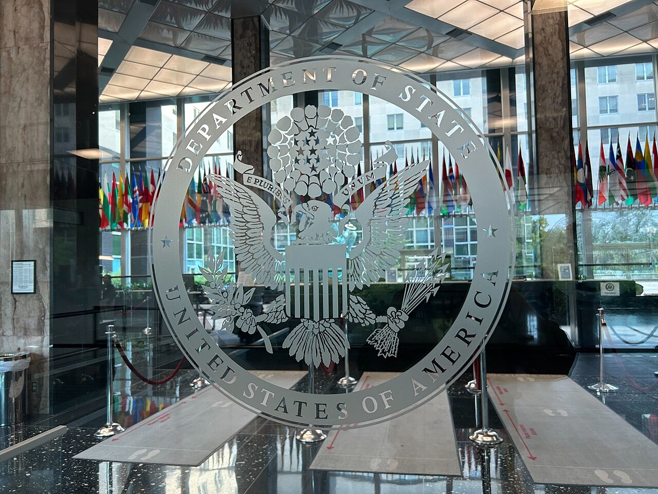 Sello del Departamento de Estado de Estados Unidos grabado en un cristal, a la entrada del vestíbulo de su sede en Washington, con banderas al fondo