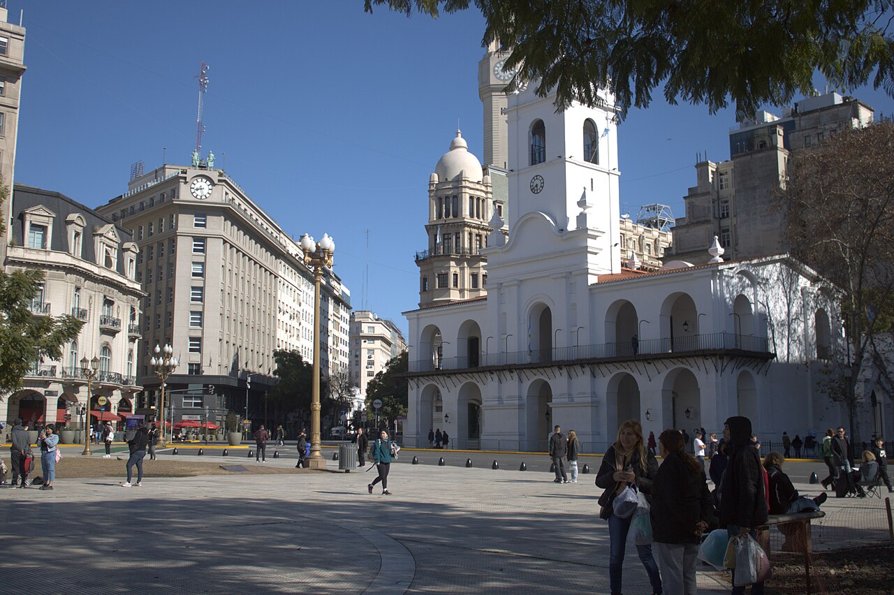 El Cabildo de Buenos Aires, edificio blanco con torre y arcadas, visto desde la Plaza de Mayo con peatones en primer plano