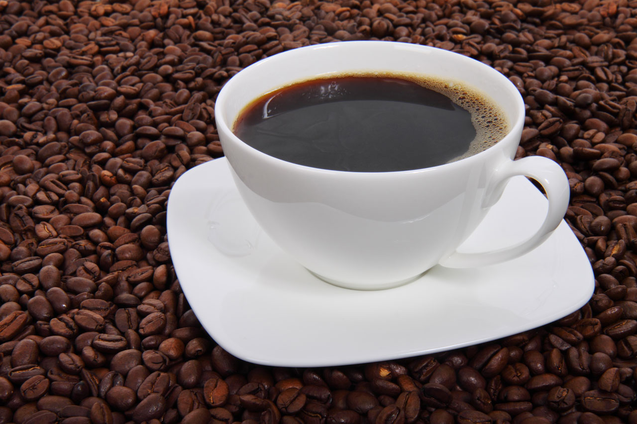 Una taza blanca de café solo sobre su plato, rodeada de granos de café tostados