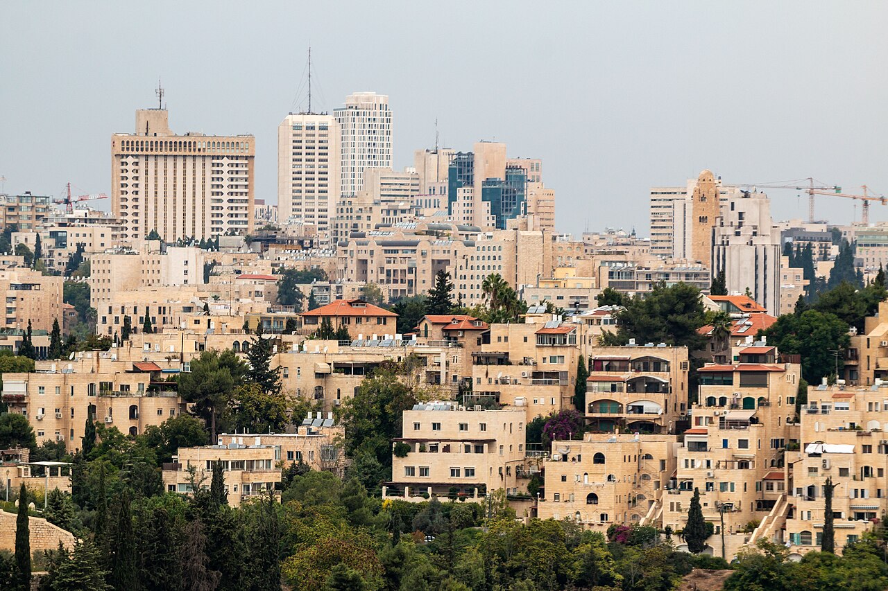 Edificios de apartamentos y torres de oficinas en el centro de Jerusalén, con árboles en primer plano y cielo gris