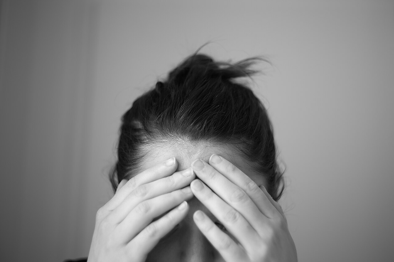 Una mujer con las manos sobre la frente y la cabeza inclinada, en blanco y negro