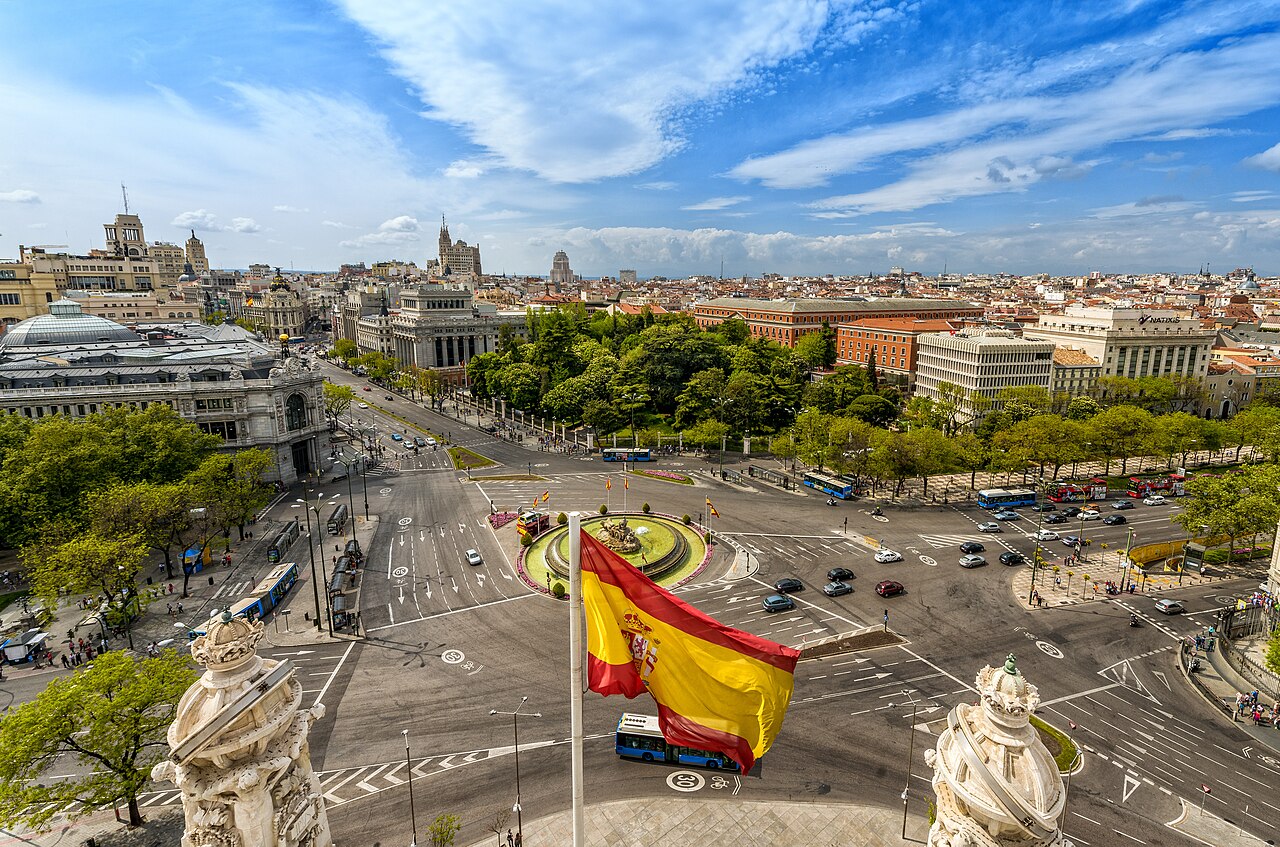 La plaza de Cibeles de Madrid vista desde lo alto, con una bandera de España ondeando en primer plano
